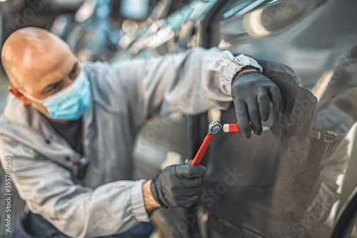 An employee of a car plant wearing a protective medical mask eliminates a small metal defect
