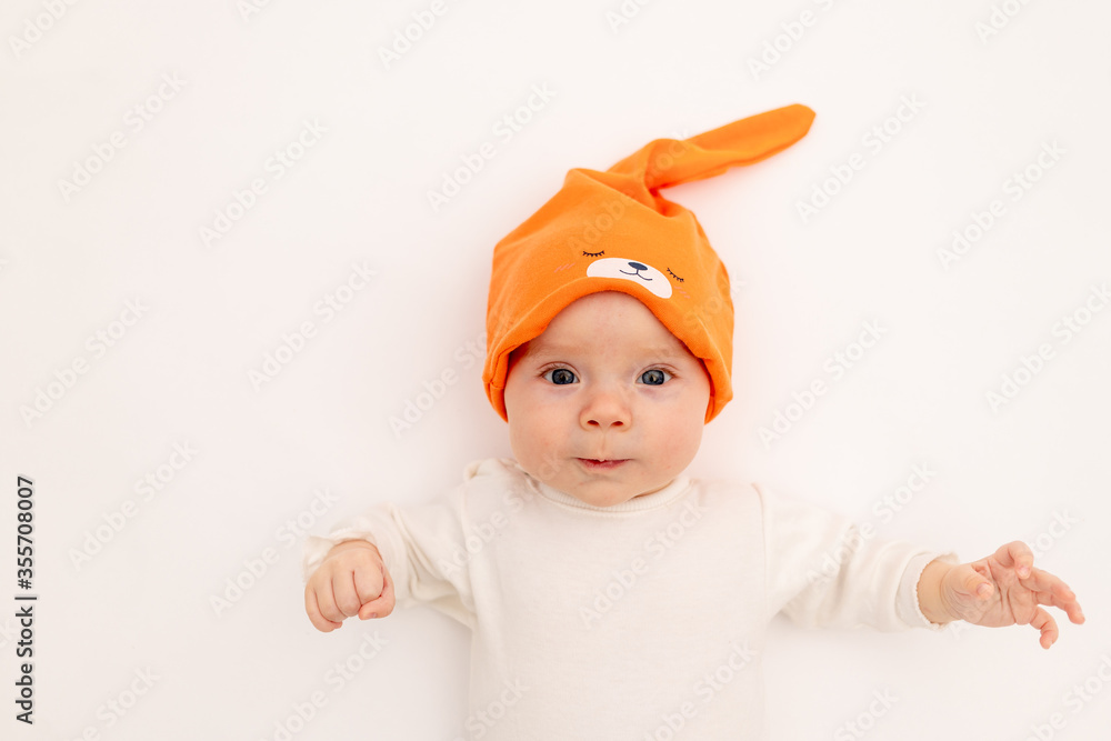 smiling baby girl in a white bodysuit in a bright orange hat on a white isolated background lies, portrait of a child 3-6 months old, space for text. A healthy happy child. smiling baby girl in a white bodysuit in a bright orange hat on a white isolated background lies, portrait of a child 3-6 months old, space for text. A healthy happy child.