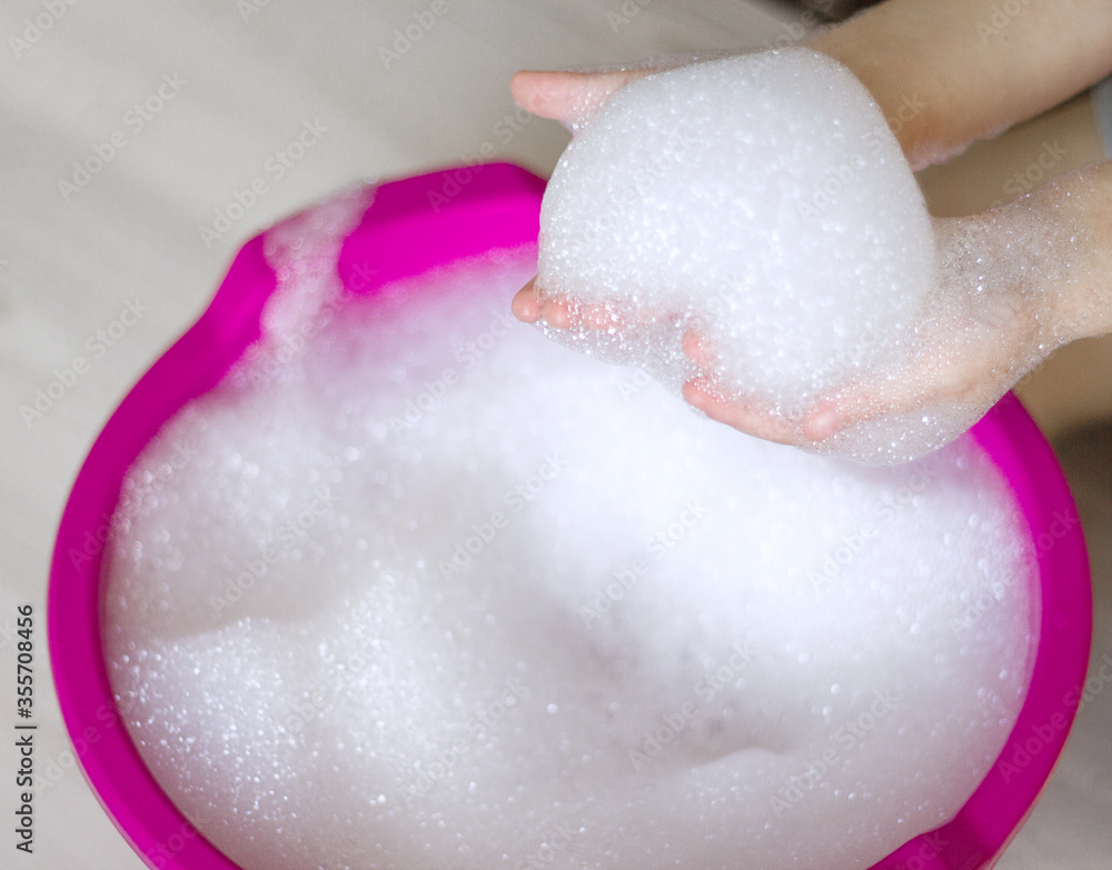Fototapeta premium Children's palms are washed in a basin with white foam, body care and personal hygiene during the period of quarantine and coronovirus, selective focus