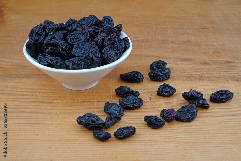 Plateful of Organic Black raisins and Spilled Black raisins on Wooden Background Plateful of Organic Black raisins and Spilled Black raisins on Wooden Background