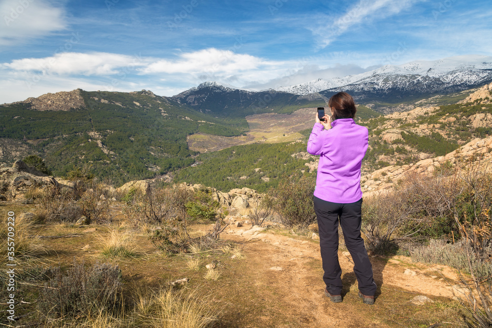 Young girl dressed in a purple fleece makes photographs of a mountain landscape with her mobile phone