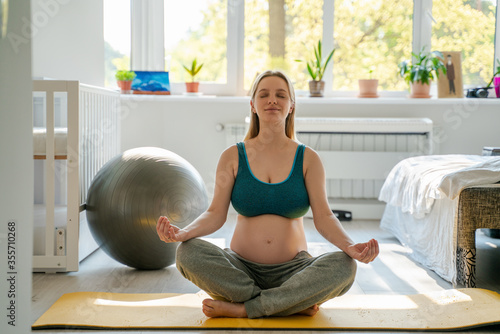 Fototapeta Naklejka Na Ścianę i Meble -  A pregnant woman at home in the morning does exercise exercises from yoga for concentration and relaxation, prepares for motherhood and the birth of a child, preparation for childbirth
