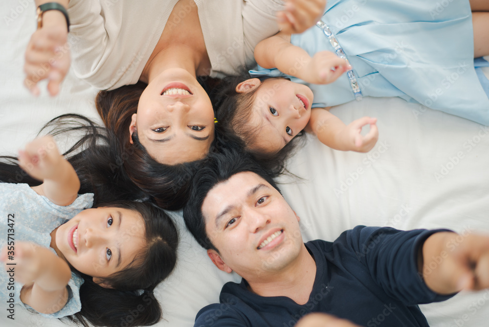 Young mother father and daughter enjoying with lying on the bed looking and point to camera, happy family smiling at home. daughter with parents playing. see from top view. Family stay at home concept