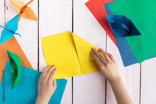A girl folds colored paper to make origami. A girl makes origami on a wooden table