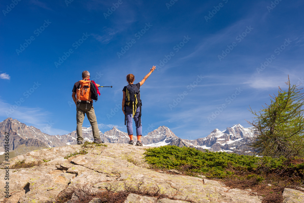Fototapeta premium Couple with backpack on mountain top. Two people looking at scenic alpine landscape summer vacation fitness wellbeing freedom concept