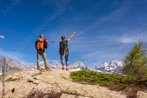 Couple with backpack on mountain top. Two people looking at scenic alpine landscape summer vacation fitness wellbeing freedom concept