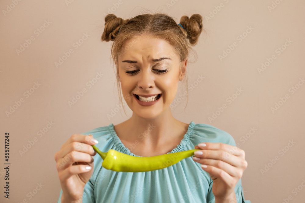 Cute woman is grimacing while holding chilli green pepper.Toned image. Cute woman is grimacing while holding chilli green pepper.Toned image.