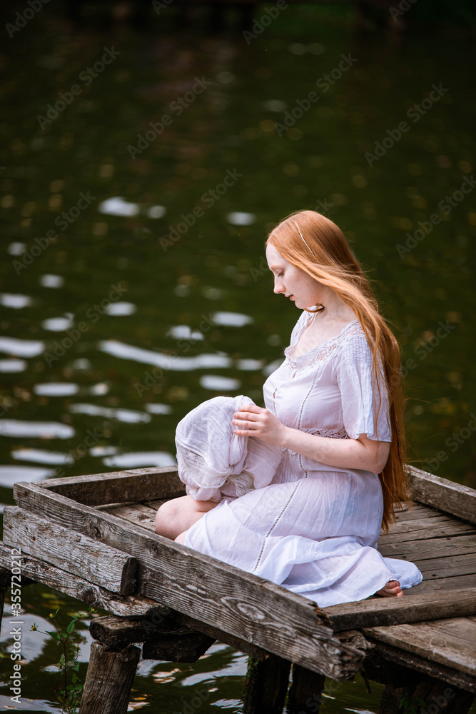 red-haired long-haired girl with freckles sits near the water on the pier