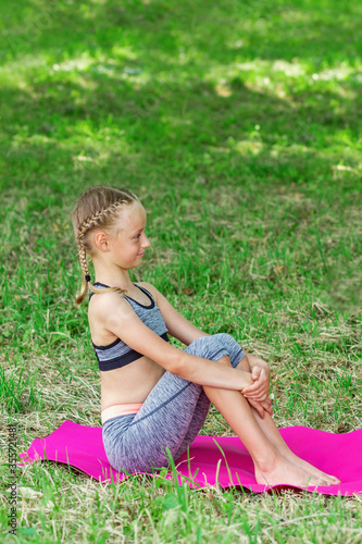 Little girl is sitting on a roll mat wearing sportswear in the public park.