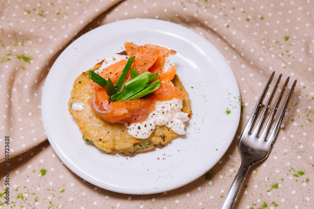 Potato pancakes with red fish on top and green onions. A portion. Small plate. Potato pancakes with red fish on top and green onions. A portion. Small plate.