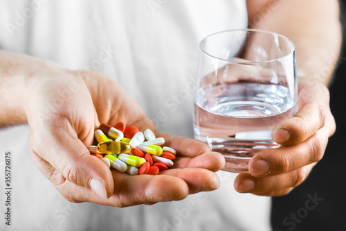 Hand holding on open palm with pill tablets medicine for healing. Man takes medicines with glass of water