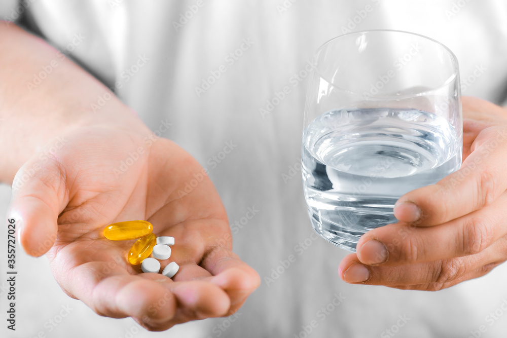 Hand holding on open palm with pill tablets medicine for healing. Man takes medicines with glass of water Hand holding on open palm with pill tablets medicine for healing. Man takes medicines with glass of water