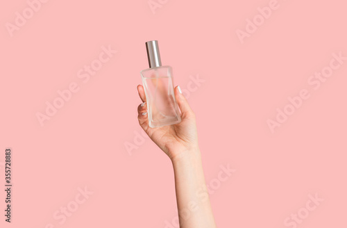 Cropped view of young girl holding bottle of perfume on pink background, closeup of hand
