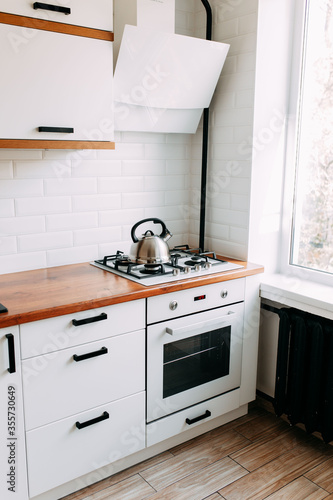 Obraz na płótnie Metallic teapot on the gas oven. Bright kitchen interior. White modern dining room. Wooden complete kitchen with gas oven. w salonie