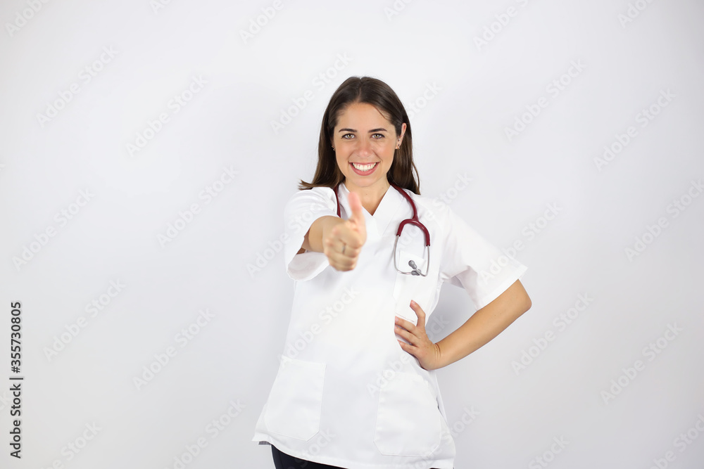 Young beautiful woman standing over white isolated background wearing her doctor uniform and doing the ok signal with her finger Young beautiful woman standing over white isolated background wearing her doctor uniform and doing the ok signal with her finger