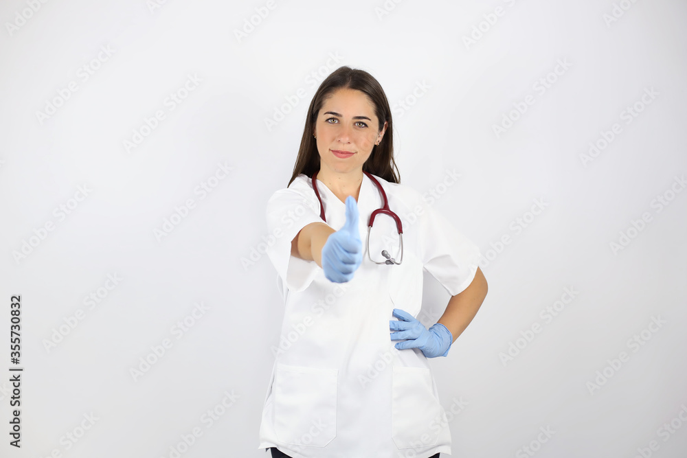 Young beautiful woman standing over white isolated background wearing her doctor uniform and doing the ok signal with her finger Young beautiful woman standing over white isolated background wearing her doctor uniform and doing the ok signal with her finger