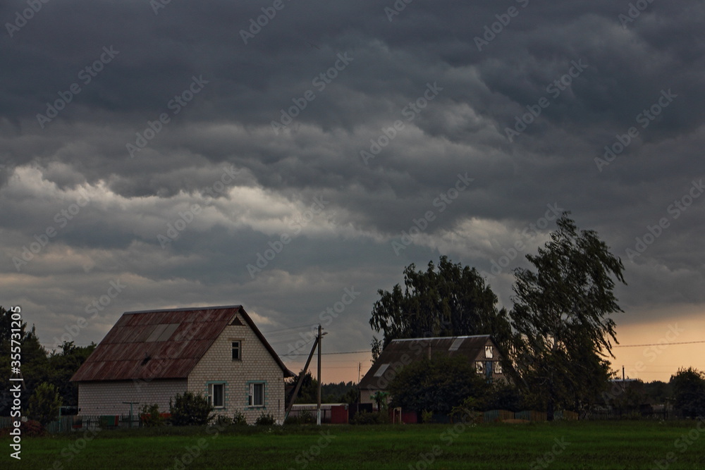 Heavy storm clouds in the dramatic sky over village house and tree on a summer evening, beautiful dramatic rural landscape