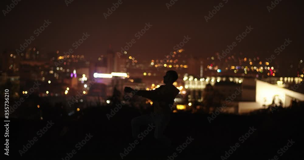 Male dancer silhouette, city lights in the background Male dancer silhouette, city lights in the background