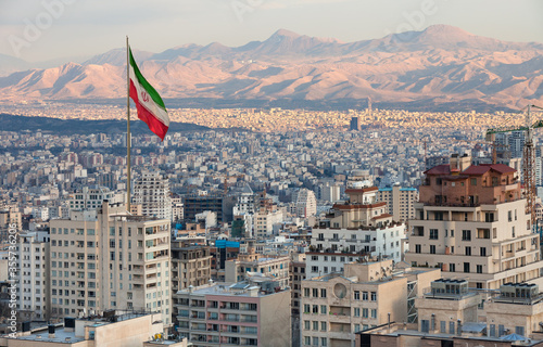 Aerial view of Tehran Skyline at Sunset with Large Iran Flag Waving in the Wind