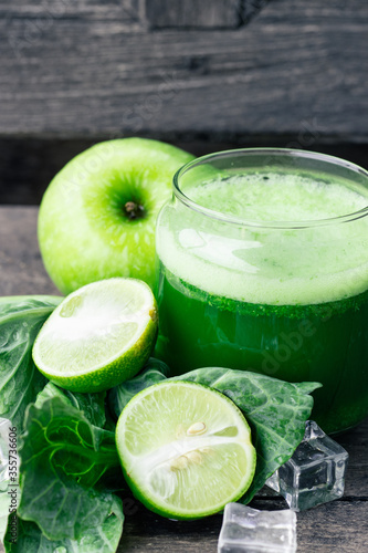 Green apple smoothie in glass and kale leaves on wooden table
