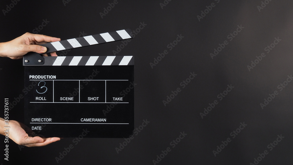 A hand is holding black clapper board or movie slate use in video production, movie, film, cinema industry on black background. It has written in number.