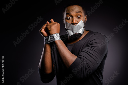 Photo of astonished afro american guy restrain arrested police hand adhesive taped lips close cover no talking speaking taboo isolated over black color background