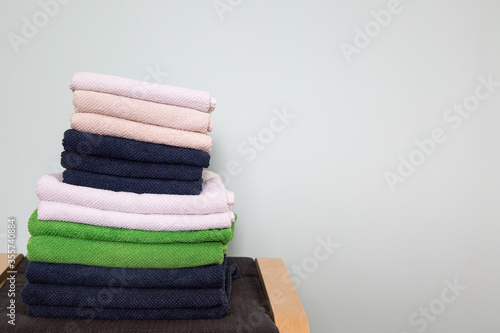 a stack of multi-colored clean towels lies on a textile-wooden stool in the room. light blue wall in the background