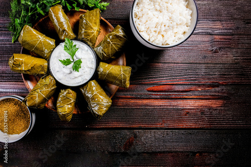 Homemade dolma on a dark wooden background with herbs, spices and sour cream sauce. Copy space