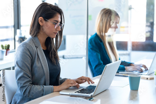Two business women work with laptops on the partitioned desk in the coworking space. Concept of social distancing.