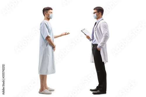 Young male patient in a hospital gown talking to a doctor and wearing protective masks