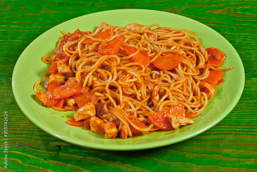 Pasta with carrots and meat in a green plate on a wooden table. Vermicelli with orange sauce on a shabby board. Pasta with carrots and meat in a green plate on a wooden table. Vermicelli with orange sauce on a shabby board.