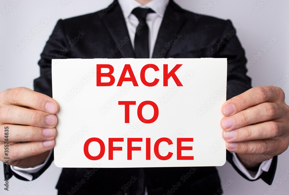 Back to office is written on a white sheet held by a businessman in a business suit. Back to office is written on a white sheet held by a businessman in a business suit.
