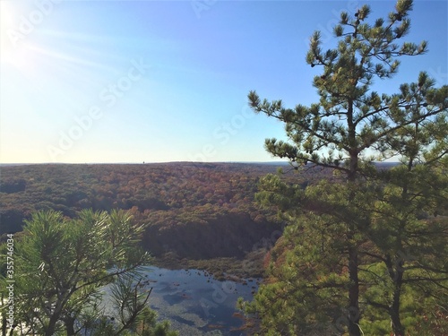 View over the edge of a cliff on a mountain on Lantern Hill trail in Connecticut, with a pond below in the distance 