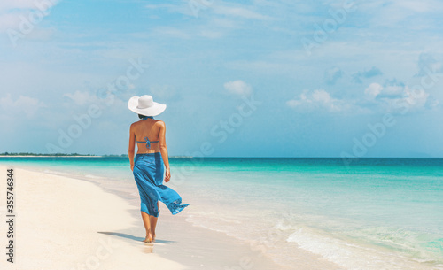 Caribbean beach vacation luxury elegant lady walking in blue beach wrap sarong skirt relaxing on idyllic holiday white sand beach stroll.