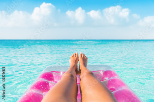 Summer relax vacation woman pov of legs relaxing on pink inflatable pool toy float floating in turquoise water ocean background. Suntan at tropical beach. photo