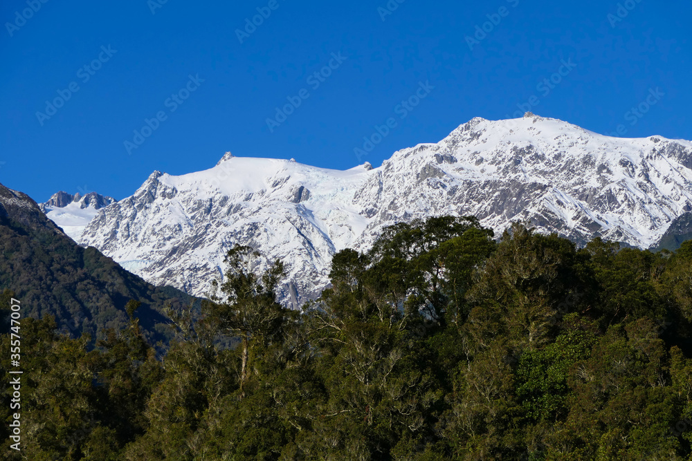 Side view of slightly snow covered mountain peaks with blue cloudless sky in early winter and trees in front