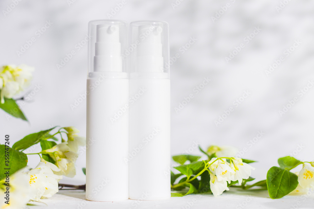 Unbranded skincare products plastic bottle with dispenser and flacons. Tube for cream shampoo. Green jasmine flowers and their shadows on the white background isolated. Mockup and copy space