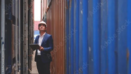 Technician or engineer worker use tablet to record data then walk around in gap of cargo container shipping workplace area with concept of good management for industrial business system.