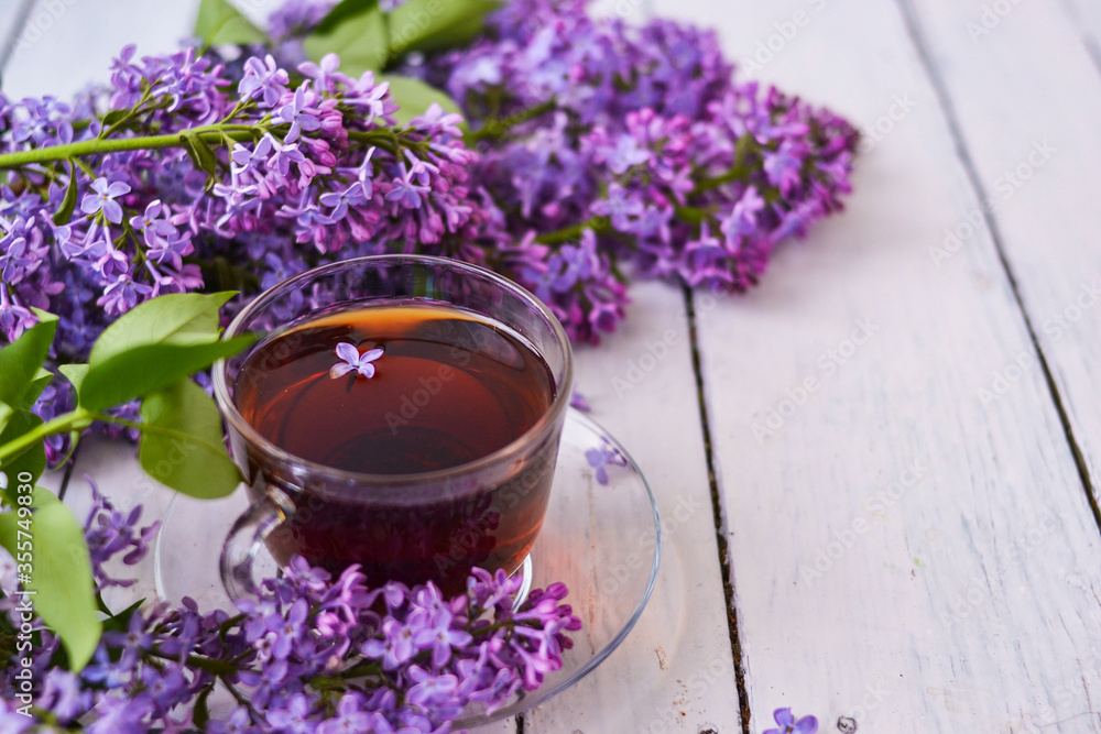 Cup of tea with lilac flowers on a wooden white background. Mocap for postcards. Spring time. Vase with lilacs. Copy space for text. The concept of holidays and good morning wishes Cup of tea with lilac flowers on a wooden white background. Mocap for postcards. Spring time. Vase with lilacs. Copy space for text. The concept of holidays and good morning wishes
