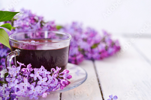 Cup of tea with lilac flowers on a wooden white background. Mocap for postcards. Spring time. Vase with lilacs. Copy space for text. The concept of holidays and good morning wishes