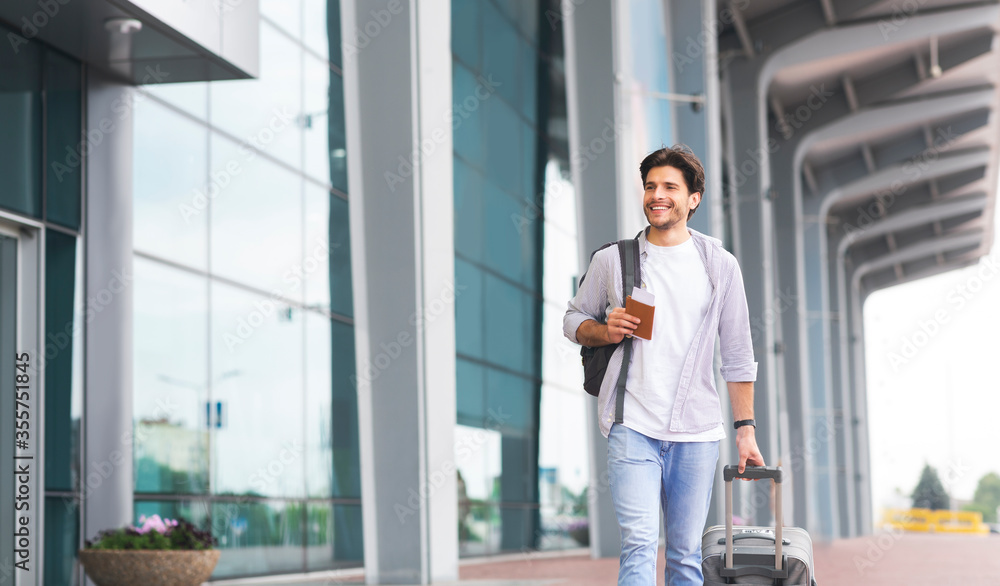 Happy man in casual wear walking near airport terminal with luggage Happy man in casual wear walking near airport terminal with luggage