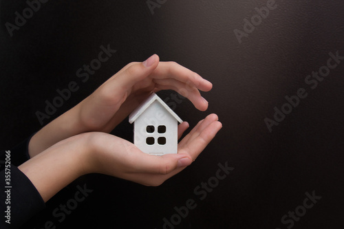 Female hands hold a small model of the house in both palms on a black background. Close-up. Copyspace