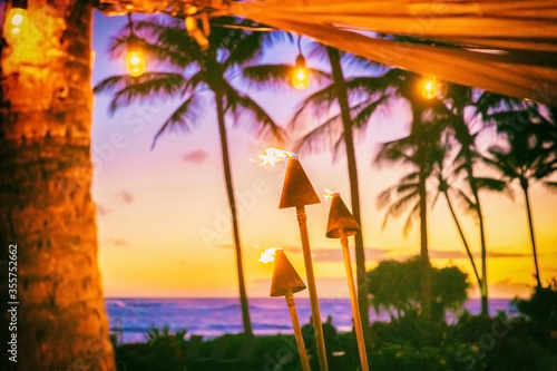 Hawaii luau party with fire torches at sunset. Hawaiian icon, lights burning at dusk at Waikiki beach resort restaurant for outdoor lighting cozy atmosphere. photo