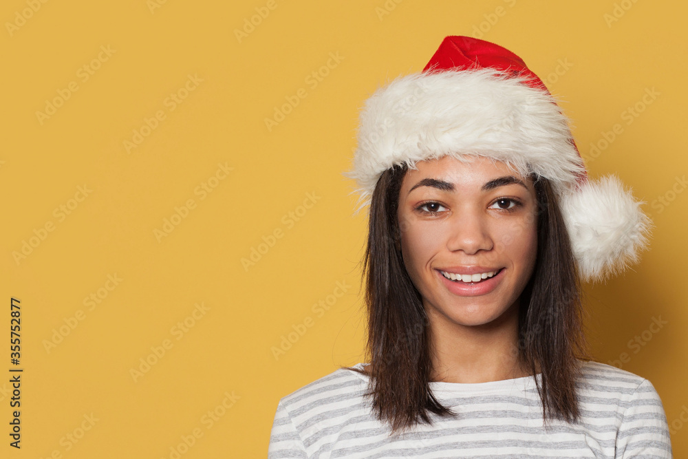Happy smiling black woman in Santa hat on yellow background Happy smiling black woman in Santa hat on yellow background