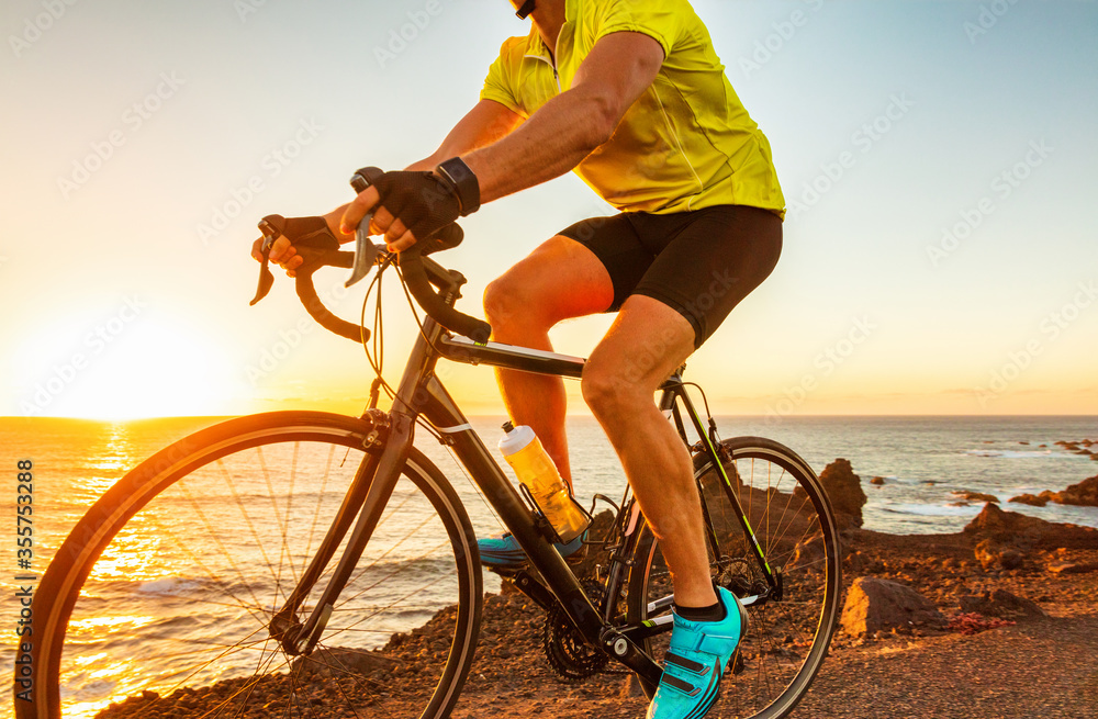 Fototapeta premium Biking cyclist riding road bike with smartwatch athlete training at sunset outdoor cycling. Sport smart watch fitness.