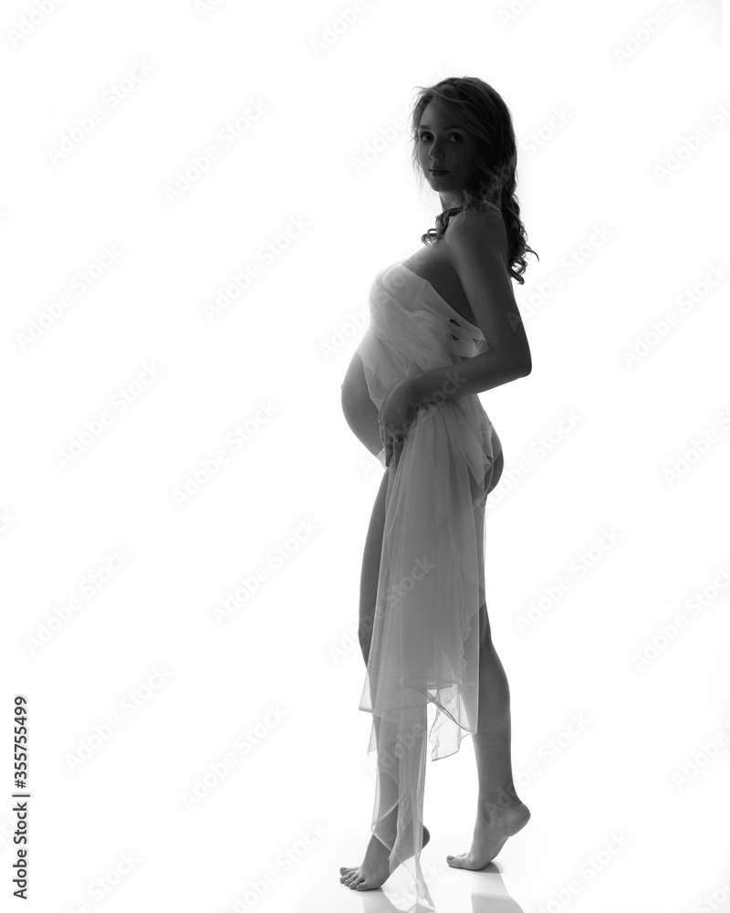 Black and white romantic image of a pregnant woman in white fabric. Pregnancy and expecting a baby concept