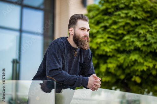 Young brutal hipster man with beard layned on handsrail near office building photo