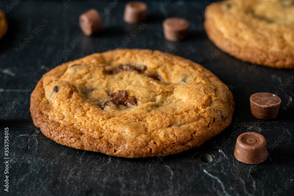 Close up of a mouth watering chocolate chip cookie with chocolate chunks shown in the background.  Food image shot in a macro style with blurred out background
