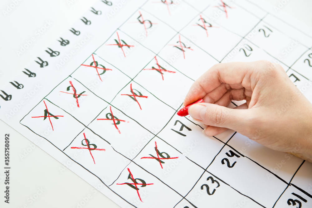Female hand counting days in hand drawn calendar with red pastel pencil Female hand counting days in hand drawn calendar with red pastel pencil