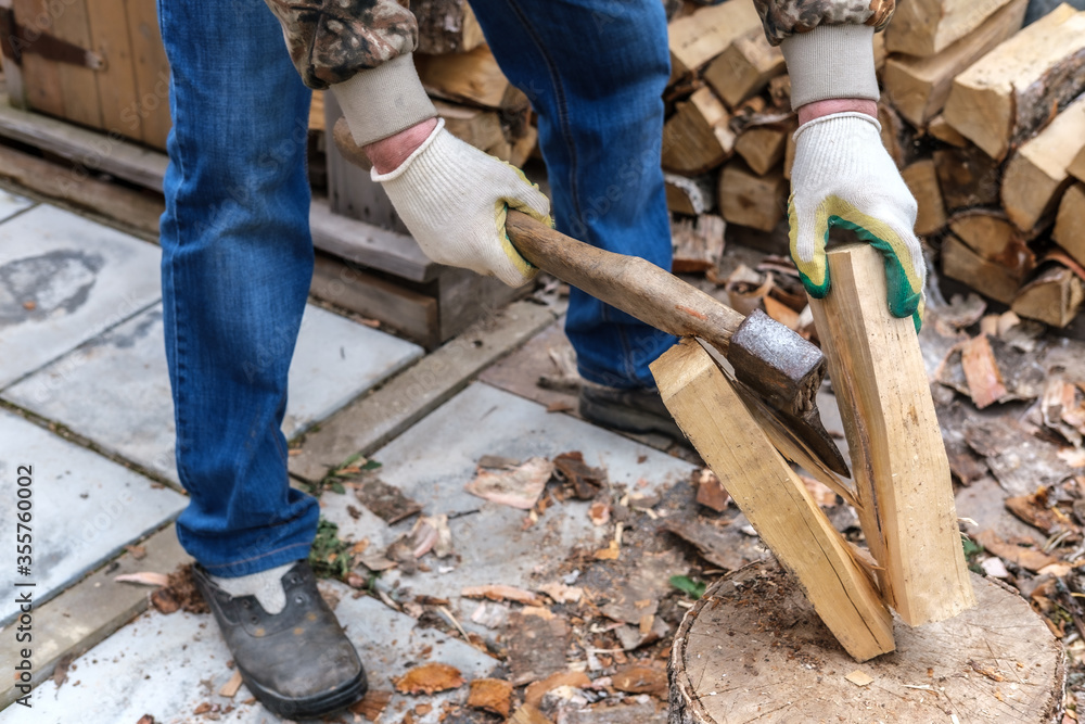 A man in gloves and blue jeans cut in half a birch log with an ax with a wooden handle. Logging firewood for the fireplace. A man in gloves and blue jeans cut in half a birch log with an ax with a wooden handle. Logging firewood for the fireplace.
